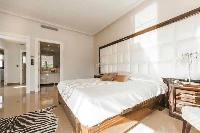 Dormitorio luminoso con cama blanca de cabecero acolchado y suelo de madera